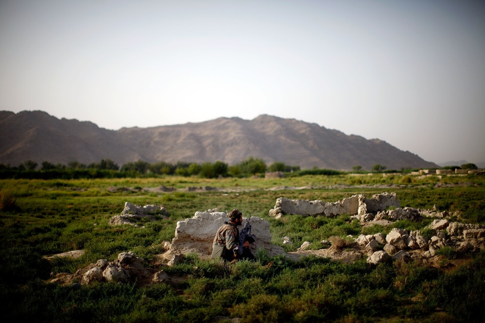 An Afghan soldier on patrol with Bravo Company crouches behind a rock after gunshots are fired.