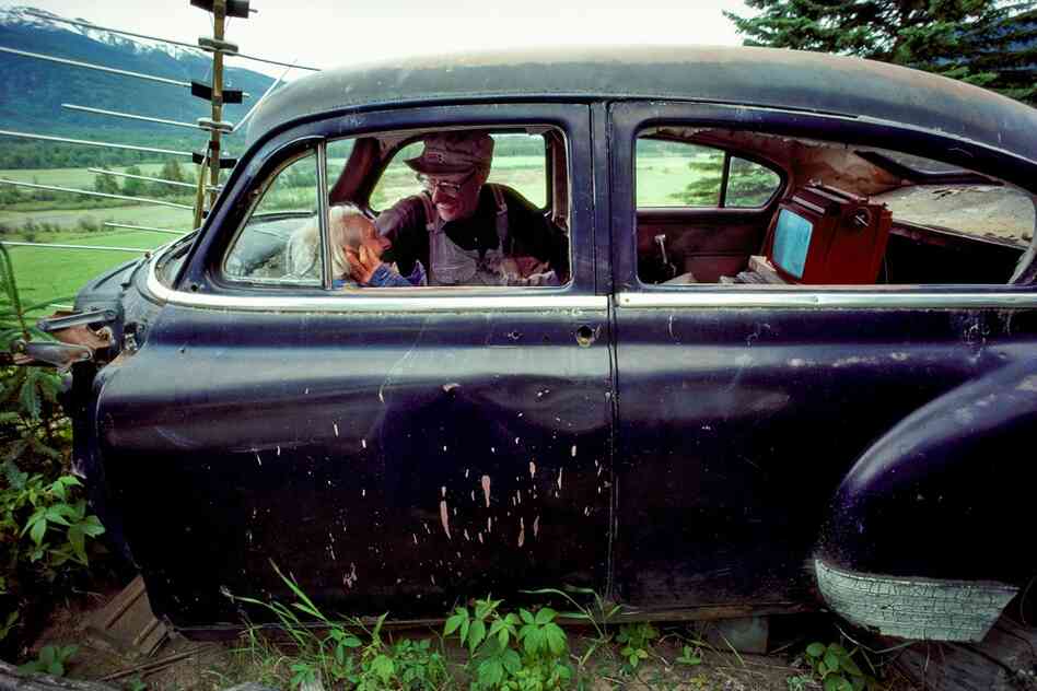 John and Josie catch up on the news in their old car on a hilltop, for better reception. McBride, British Columbia, Fraser River, Canada.. 