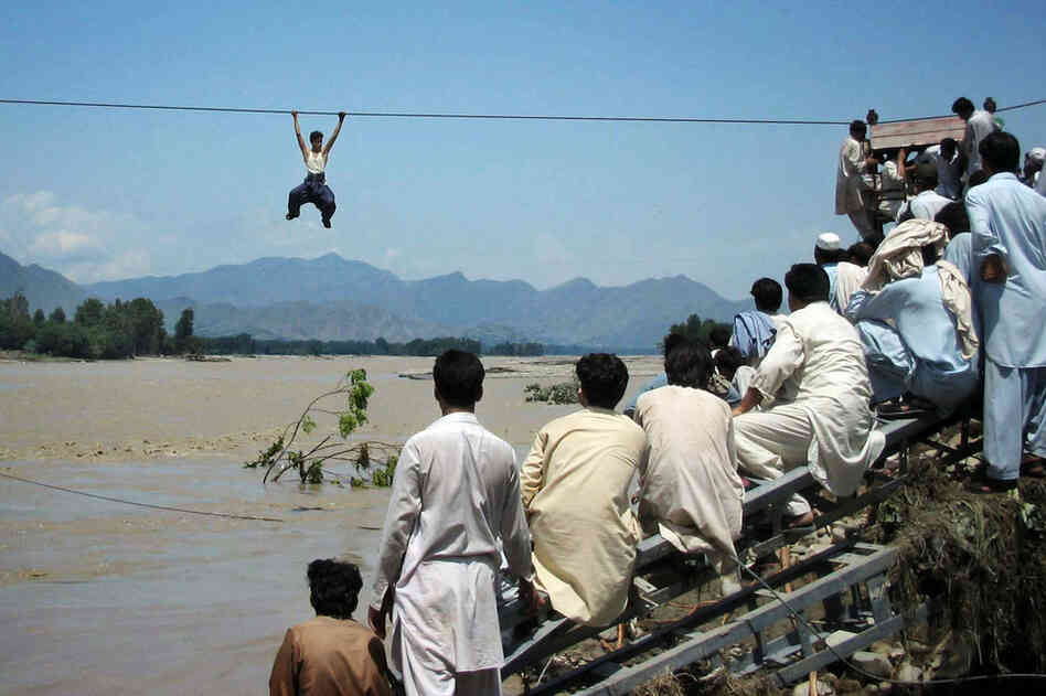 Onlookers perched on a damaged bridge watch a man cross a river by rope Aug. 3 in Swat Valley's Chakdara. 