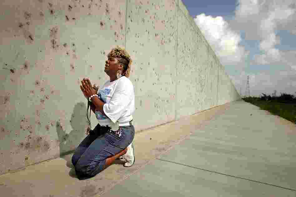 Oblique Weaver, who lost four family members during Katrina, kneels in the Lower 9th Ward at the repaired levee wall that was breached in the storm's aftermath. Weaver was attending the Great Flood memorial ceremony and march Aug. 29, 2006, one year after the storm. 