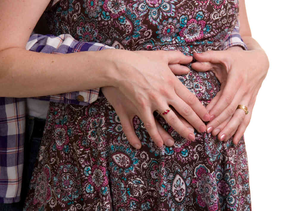 A young couple expecting their first child - hands held in shape of heart of her belly. A young couple expecting their first child - hands held in shape of heart of her belly.