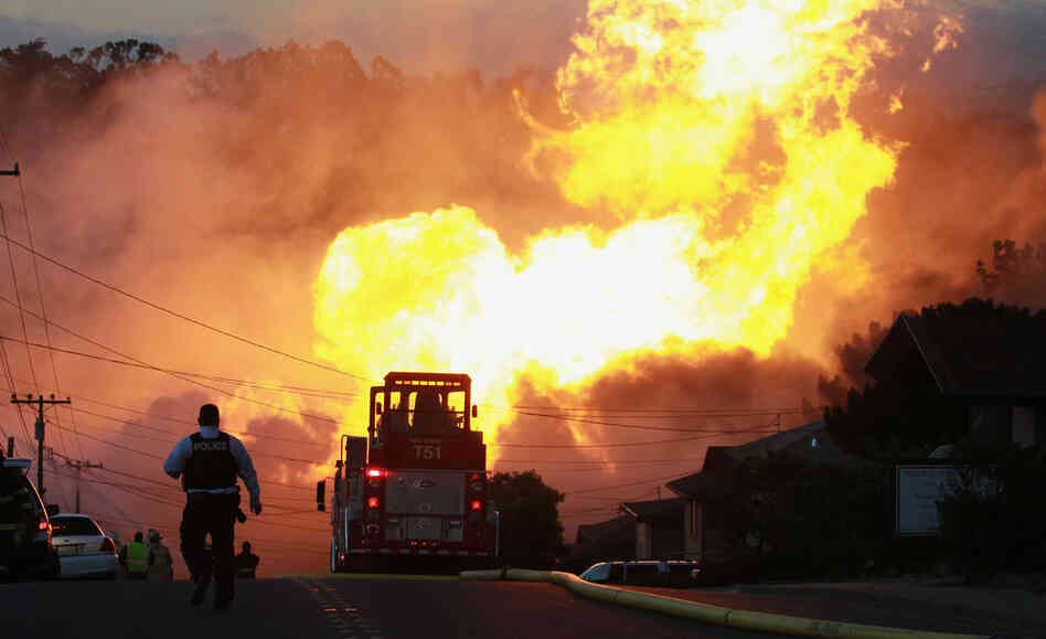 A law enforcement official runs towards a massive fire in a residential neighborhood. 