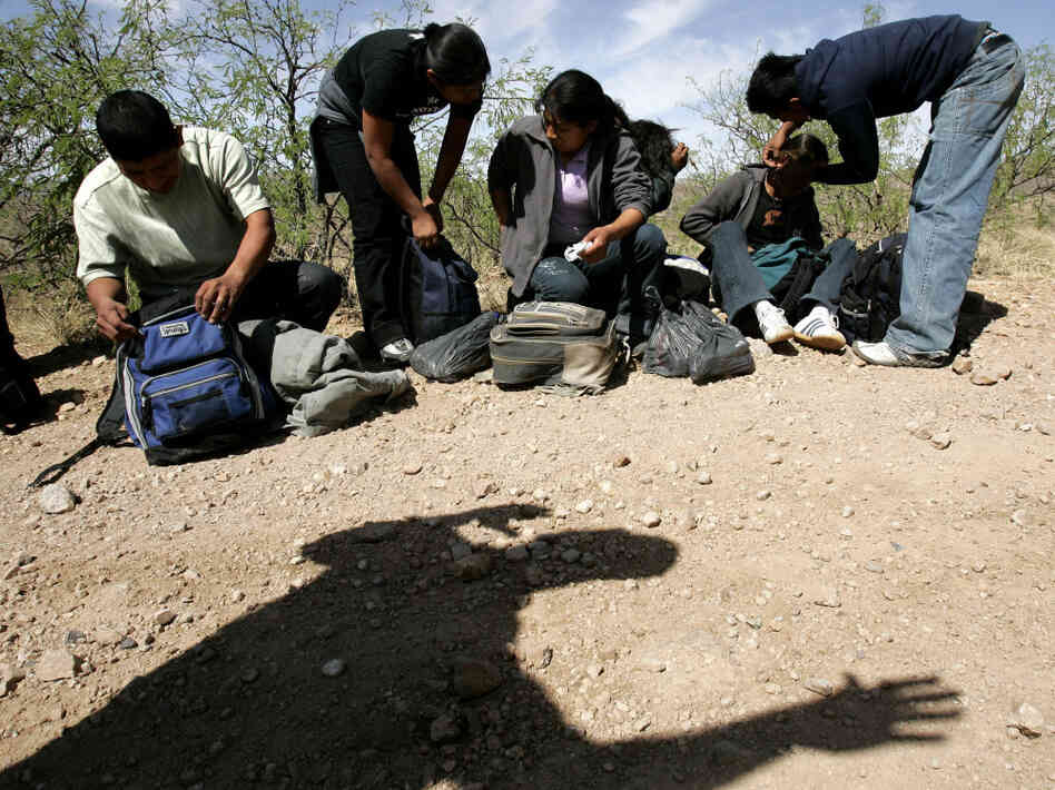 A U.S. Border Patrol agent casts a shadow below a group of migrants detained near Arivaca, Ariz.