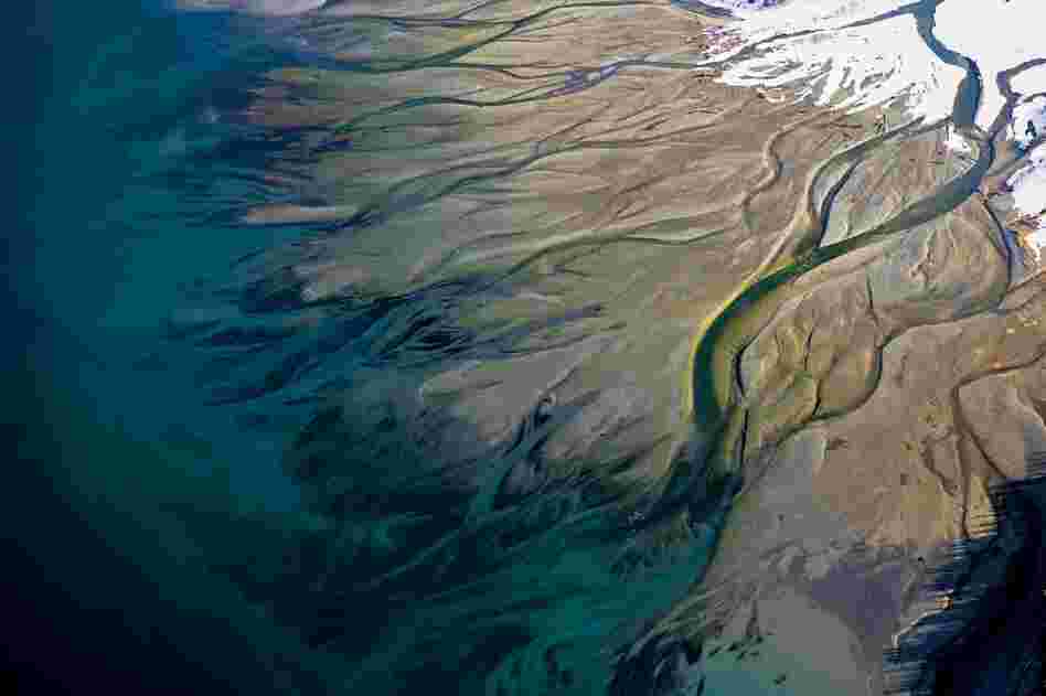 Tributaries of Lynn Canal, a spectacularly deep fjord in Alaska, wind across a muddy plain to empty into a blue-green bay.
