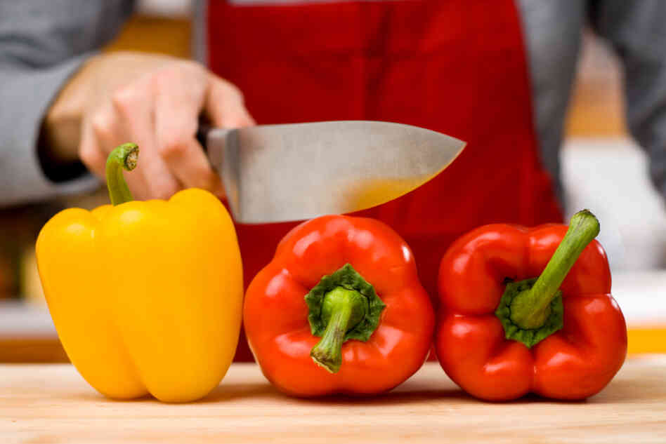 A woman holds a knife over a red pepper. A woman holds a knife over a red pepper.