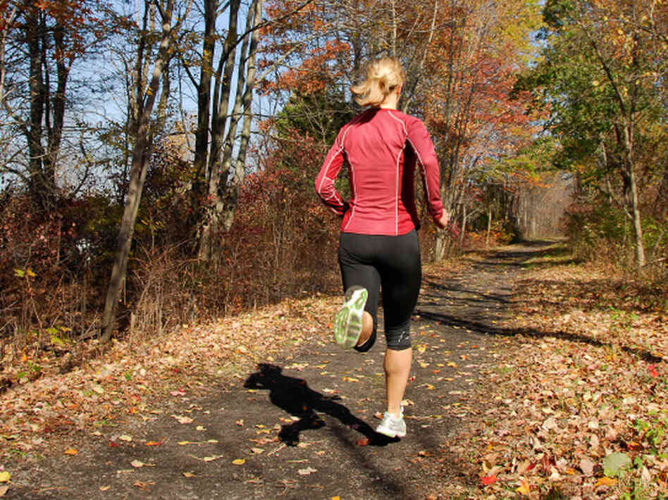 A woman runs along a dirt road in the woods. A woman runs along a dirt road in the woods.