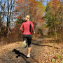 A woman runs along a dirt road in the woods.