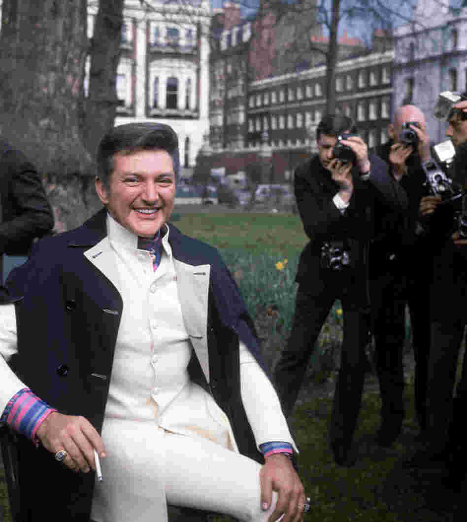 Liberace holds the attention of a group of photographers in a London park.  
