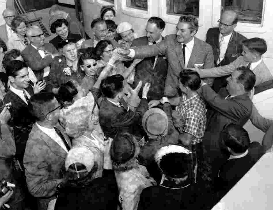 Surrounded by well-wishers, Liberace shakes hands with a fan as he and his brother and manager, George, sail from New York to Europe on the liner Queen Mary in September 1956. 