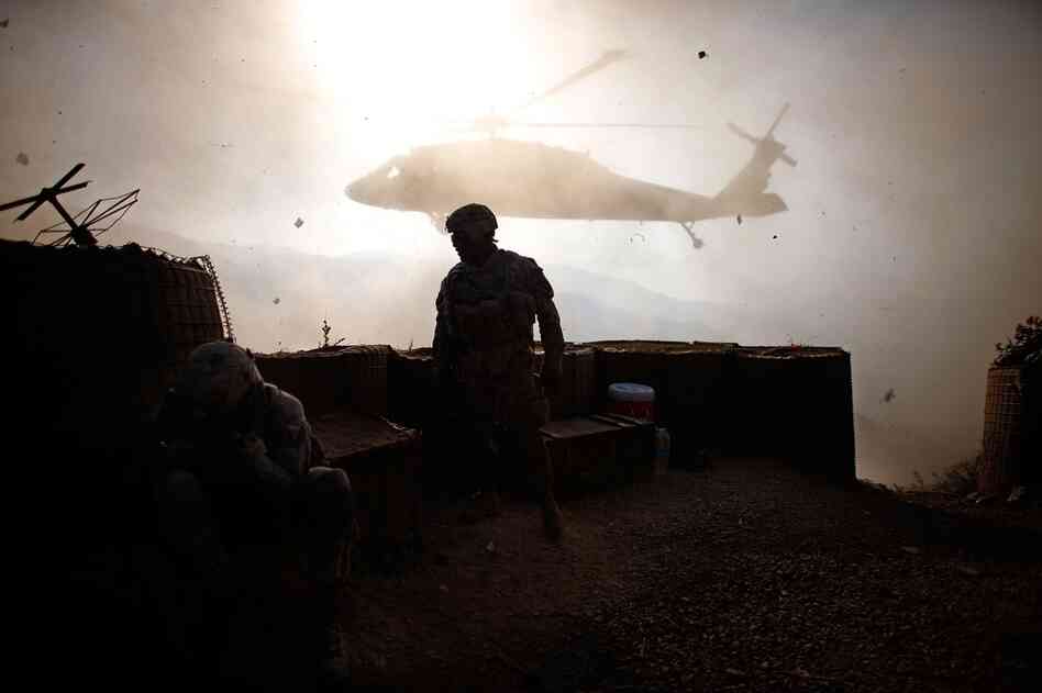 The following morning, Sgt. 1st Class Cliffton Robinson (center) of Alpha Company stands in the dust and debris of the rotor wash from a Black Hawk helicopter at the Ghakhi Pass. U.S. troops head back to the landing zone early and remove the downed helicopter.