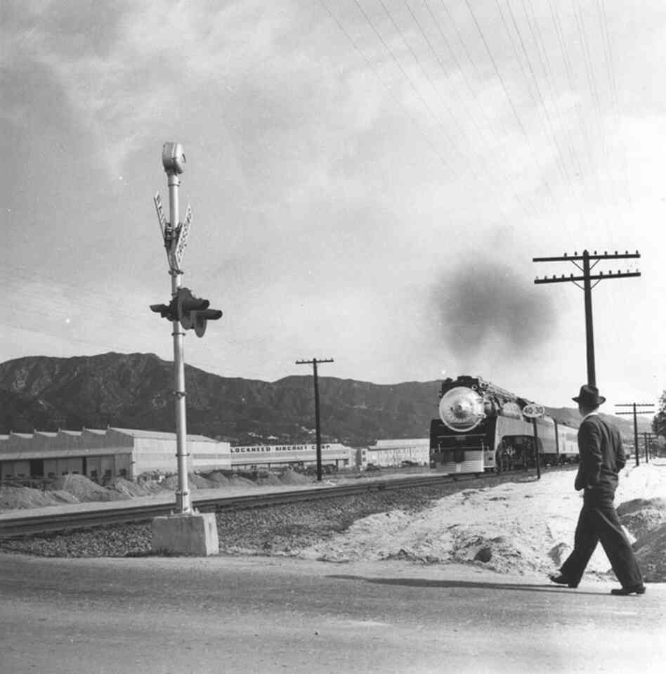 A man walks on an unidentified Burbank street. The Lockheed Aircraft plant and the Verdugo Mountains are seen in the background.