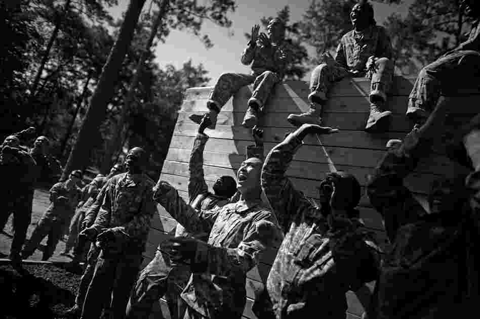 Soldiers cheer and jeer for private trying to make it over the highest wall on a climbing exercise and obstacle course.