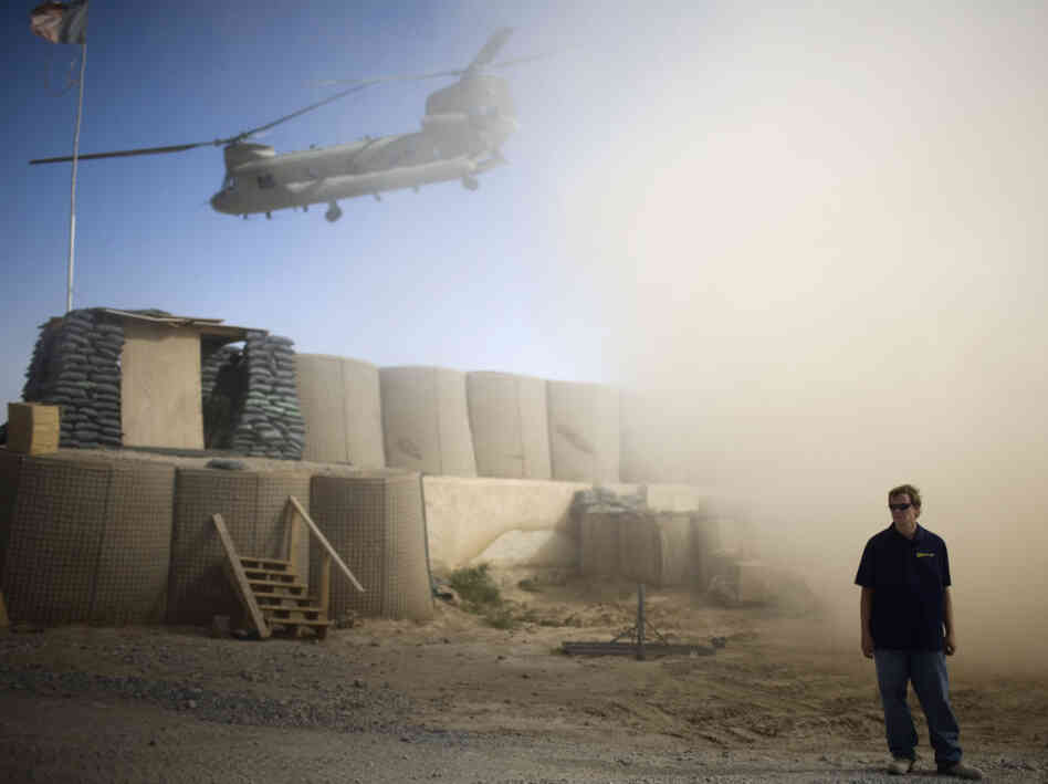 A U.S. contractor looks away from a dust cloud whipped up by a helicopter.