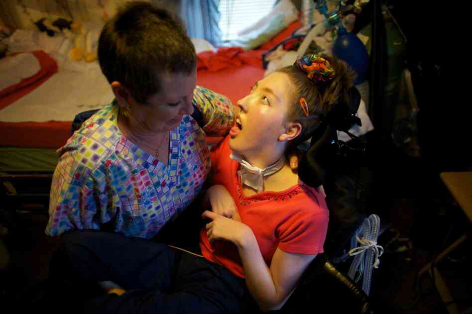 Nurse Helen Houchins moves Welter from her bed to a wheelchair.  Welter needs 24-hour care and she breathes with the help of the portable ventilator on the back of her wheelchair. She can't speak, can't move and can't even close her eyelids — her eyes are wide open.