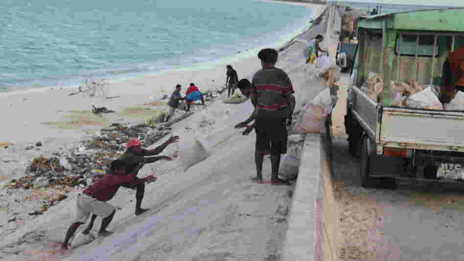 People mine bags of sand along a causeway in South Tarawa. People mine bags of sand along a causeway in South Tarawa.