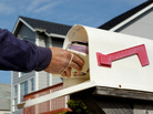 A letter carrier delivers a bundle of mail to a mailbox A letter carrier delivers a bundle of mail to a mailbox