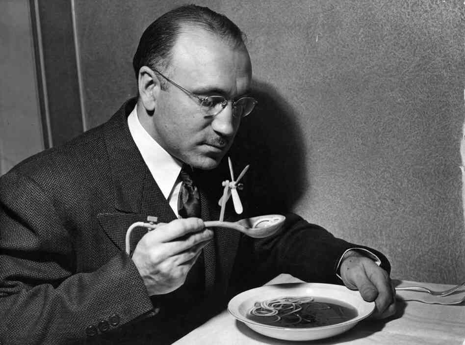 A man eating soup with a mechanical soup spoon. The device is intended for dinner parties where the hostess serves inedible soup. The offending soup is drained through a hollow handle, via a tube hidden up the sleeve, into a bottle attached to the leg. Foul odours are blown away by the propeller. The innocent hostess believes the device is simply for cooling her delicious fare. (Hans Reinhart/K...