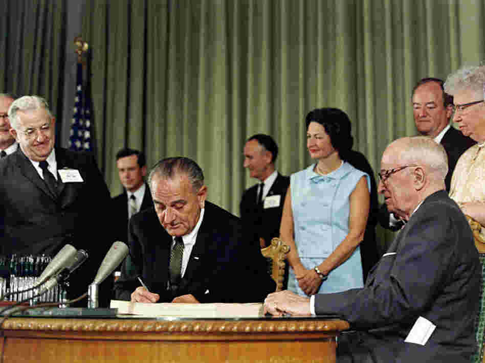 President Johnson (center) signs the Medicare Act in 1965 as Harry Truman (right) looks on.