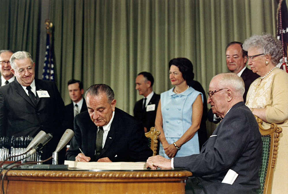 President Johnson (center) signs the Medicare Act in 1965 as Harry Truman (right) looks on.