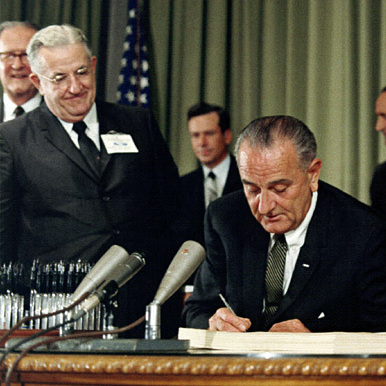 President Johnson (center) signs the Medicare Act in 1965 as Harry Truman (right) looks on.