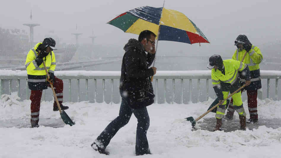 A pedestrian passes men shoveling snow in Lyon, France. Heavy snow and subzero temperatures have s A pedestrian passes men shoveling snow in Lyon, France. Heavy snow and subzero temperatures have s