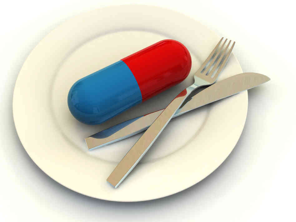 A giant pill sits next to a knife and fork on a dinner plate. A giant pill sits next to a knife and fork on a dinner plate.