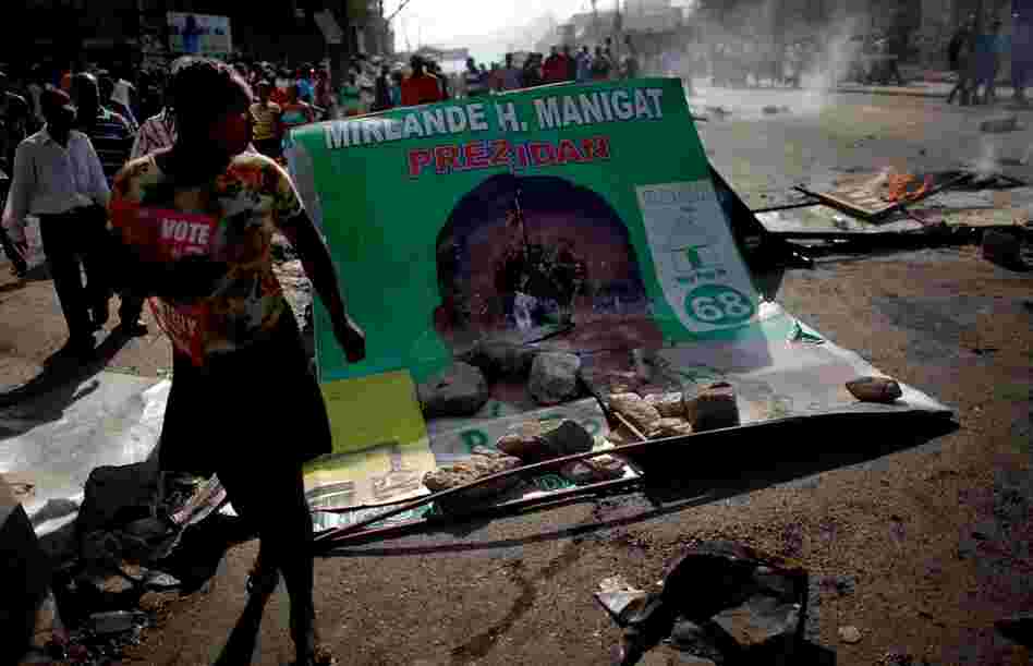Martelly supporters take to the streets, walking past a smashed billboard of Manigat.