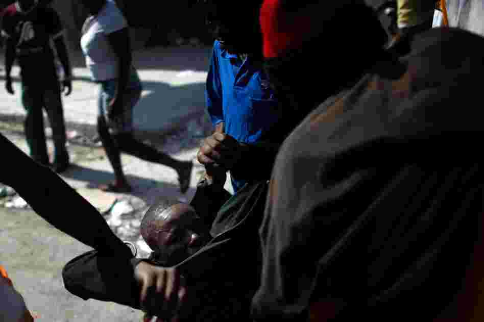 U.N. peacekeepers and the joint Organization of American States-Caribbean Community observer mission say the election problems do not invalidate the vote. Here, protesters help an injured man who was hit in the head with a rock.