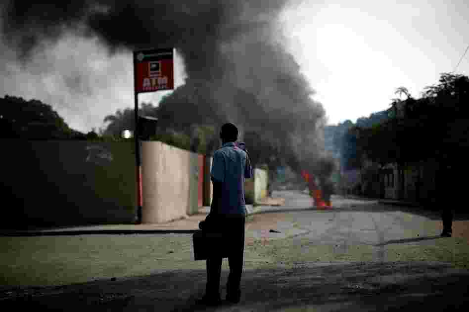 A Haitian man takes a photo of the destruction with his cell phone. Protests began as soon as the election news was announced.