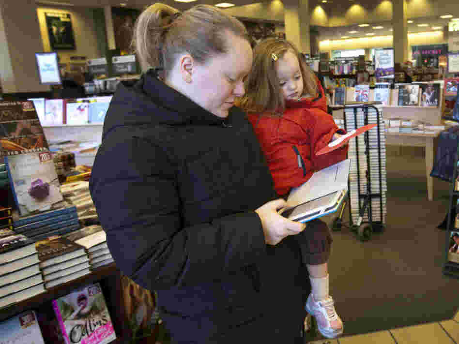 Emily Fernandez, holding her daughter Bethany, uses her Nook e-reader to browse some books.