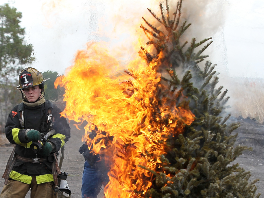 A fire department cadet monitors a Christmas tree on fire during a holiday safety demonstration.