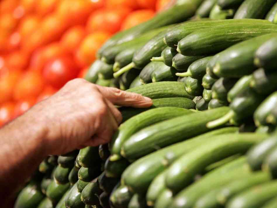A worker fills the vegetable shelves with organic cucumbers at a supermarket. A worker fills the vegetable shelves with organic cucumbers at a supermarket.