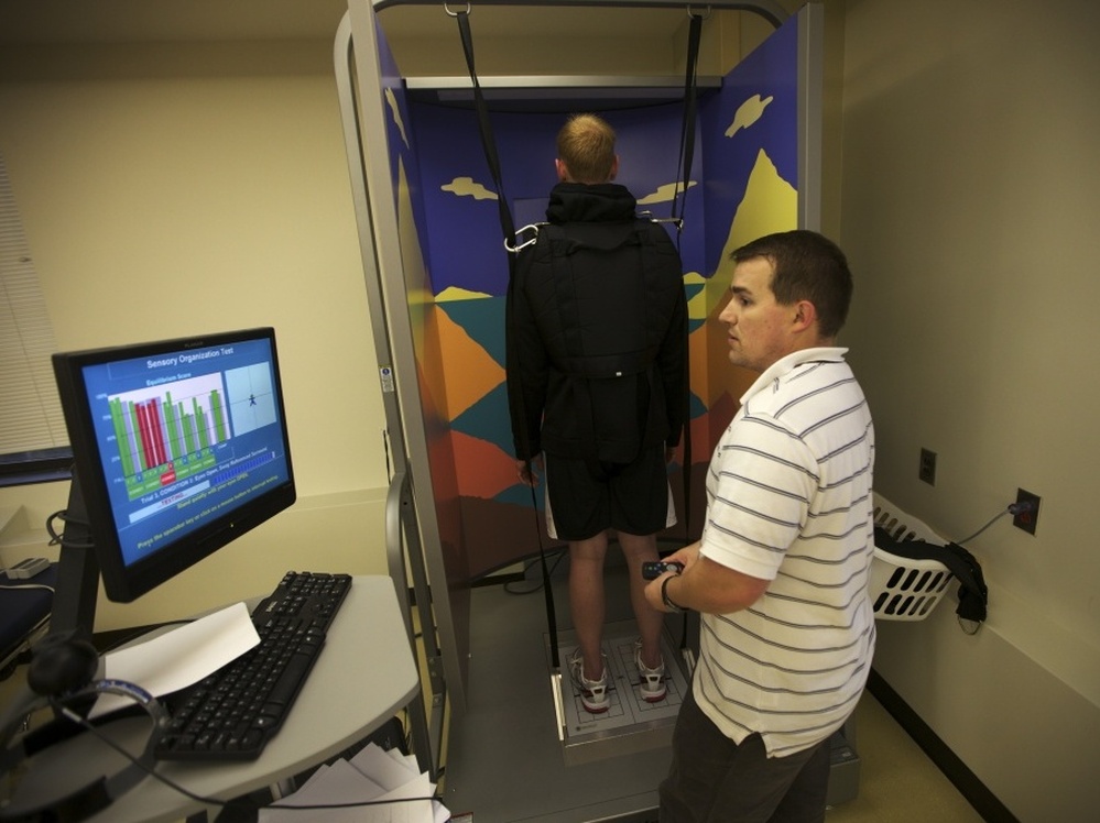 Brendan Jannesen, 23, works with Brian Smith (right), a physical therapist, on issues with his knee. Jannesen, who was injured in Afghanistan while working as a Forward Observer for the Army, is strapped into a machine that measures his body's responses to abrupt balance changes. 