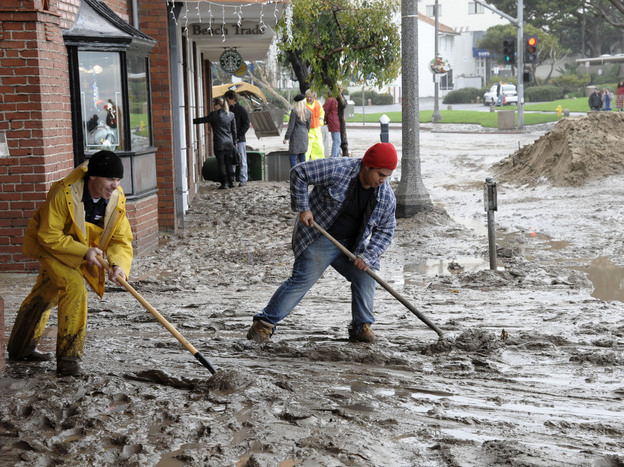 Workers shovel mud out onto Pacific Coast Highway from the Laguna Cinemas in Laguna Beach, Calif.