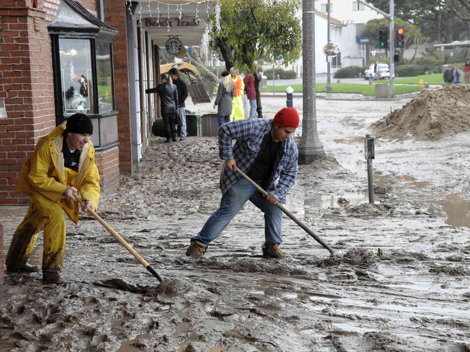 Workers shovel mud out onto Pacific Coast Highway from the Laguna Cinemas in Laguna Beach, Calif.