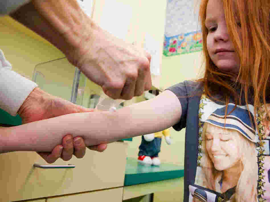 A nurse applies a numbing cream to Katie's arm so she can draw blood to check her lead level. Katie's lead level has gone down since her last visit but, as she goes through a growth spurt, her bones release more lead into her blood.