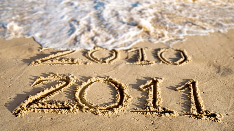 An ocean wave washes away the year 2010 written in beach sand.