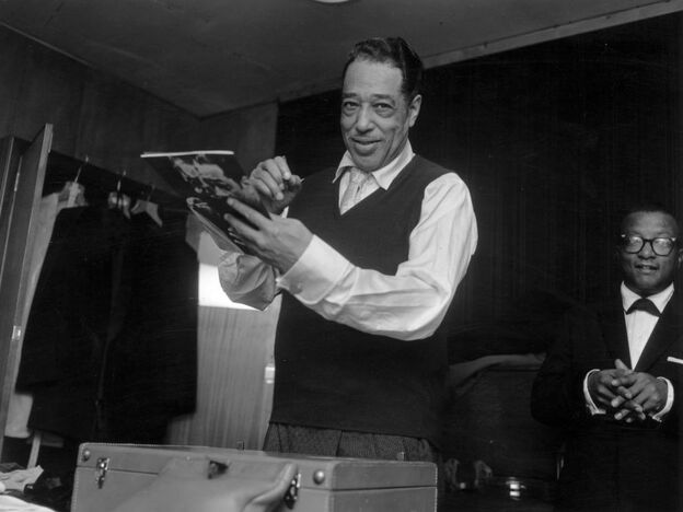 Duke Ellington signs his biography in London in 1958, with Billy Strayhorn in the background.
