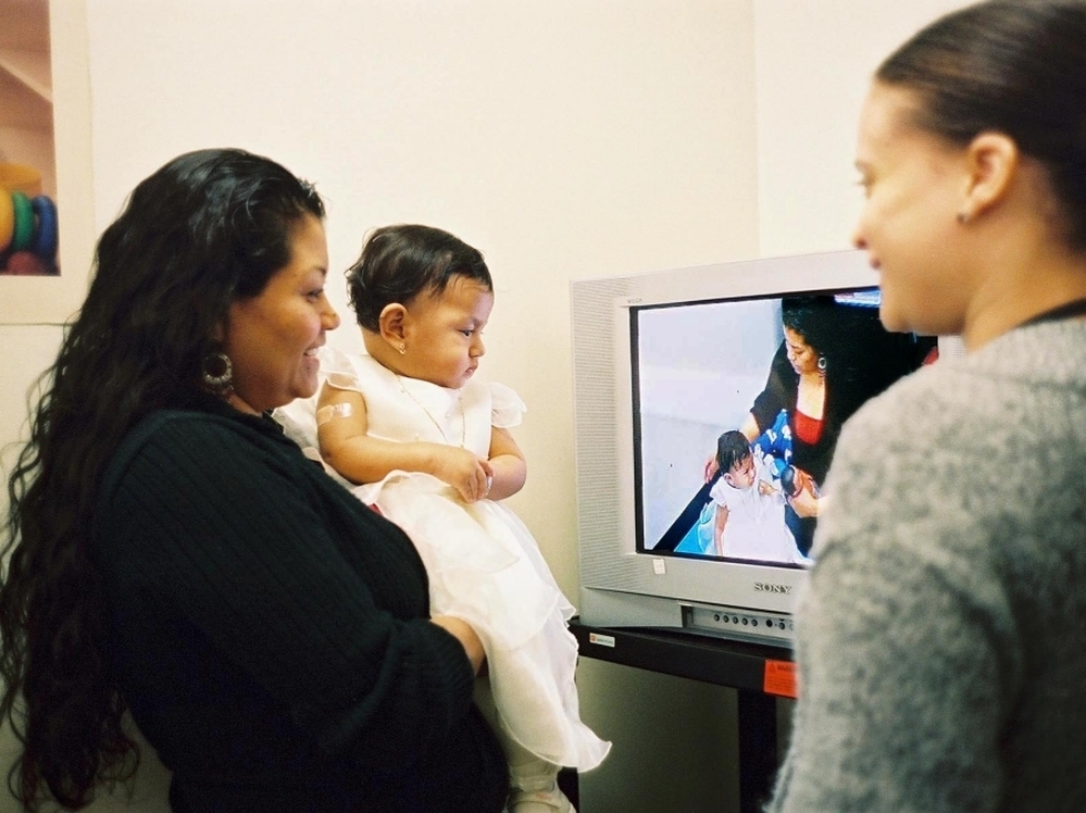 A mother watches a video taken of herself playing with her daughter for Bellevue Hospital's Video Interaction Project. Former hospital employee Brenda Woodford reviews the footage, offering positive feedback and areas for improvement.