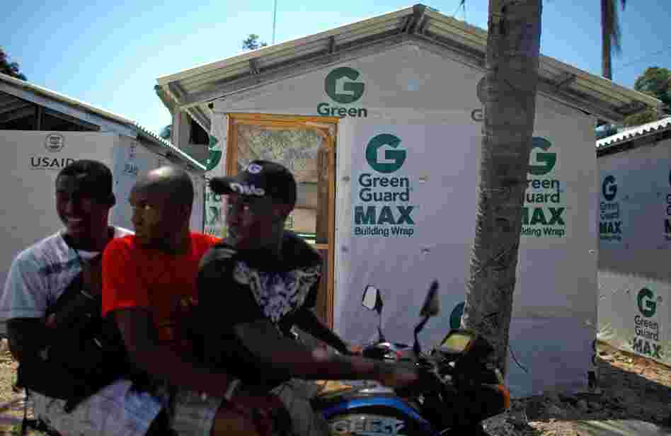 Four months after the earthquake, a group of Haitians ride by one of the pre-fabricated houses being built for people in Leogone, Haiti. The houses are a temporary solution to the long-term problem of rebuilding, May, 2010.