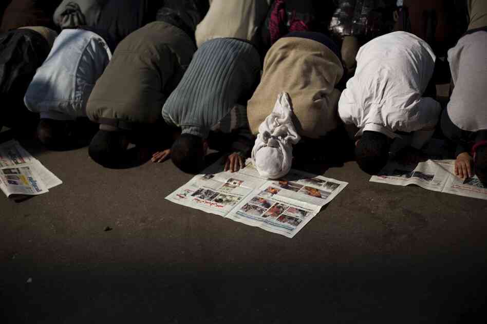 Anti-government protesters pray next to newspapers with the latest local news in Tahrir Square. 