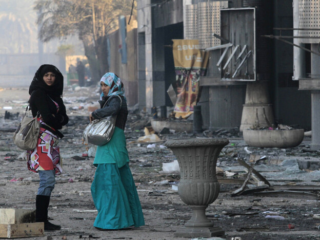 Women in Cairo walk past a shopping center Monday that was damaged during the anti-government uprising.