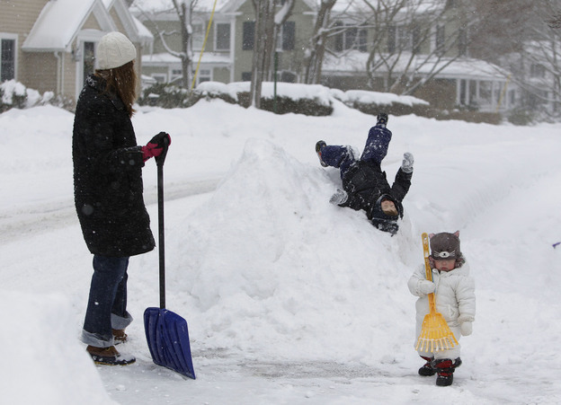 William Chisholm, 2, slides down a snow bank in front of his house as he mother, Tara looks on and his younger sister Ilona, 13 months, helps her mom shovel using a rake in Cohassett, Mass. The first half of a two-part winter storm is expected to drop up to a foot of snow in parts of New England Tuesday before a second storm slams into the area Wednesday.