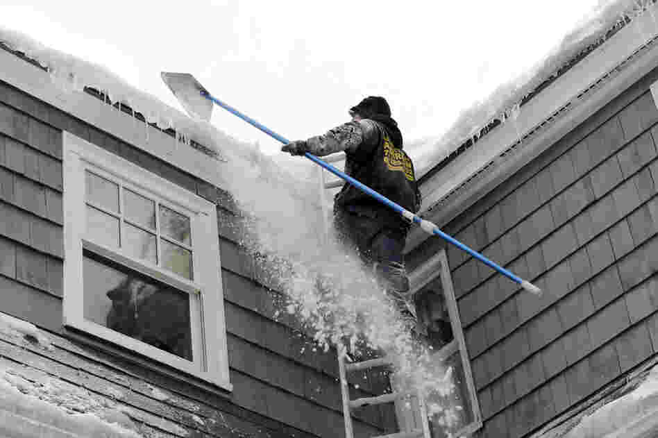 Andrew Santino of Santino's Roofing uses a rake to clear snow from a residential roof in Andover, Mass., on Wednesday. 