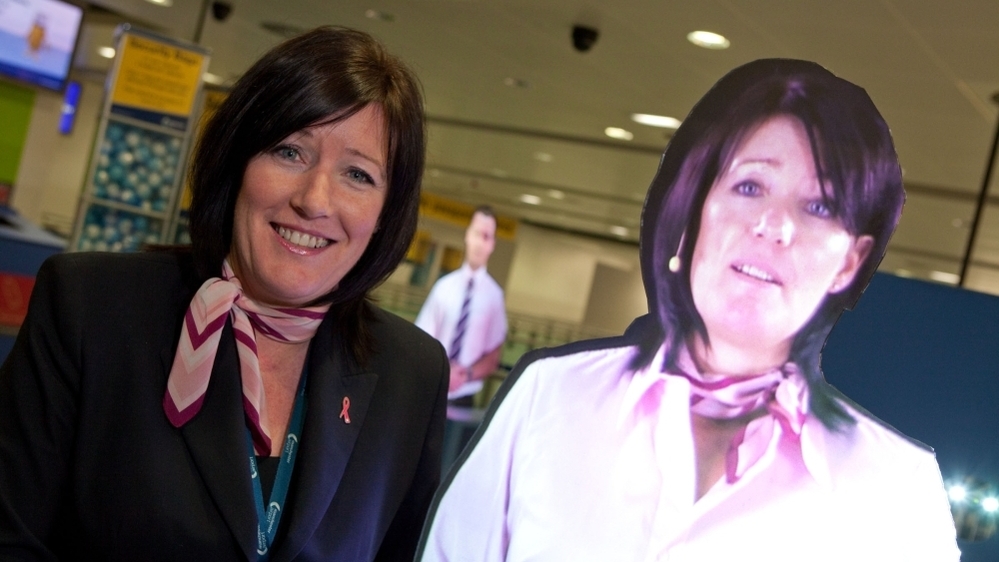 Julie Capper stands with her hologram at Manchester International Airport. Julie and her hologram work in the same area — which has created some confusion.