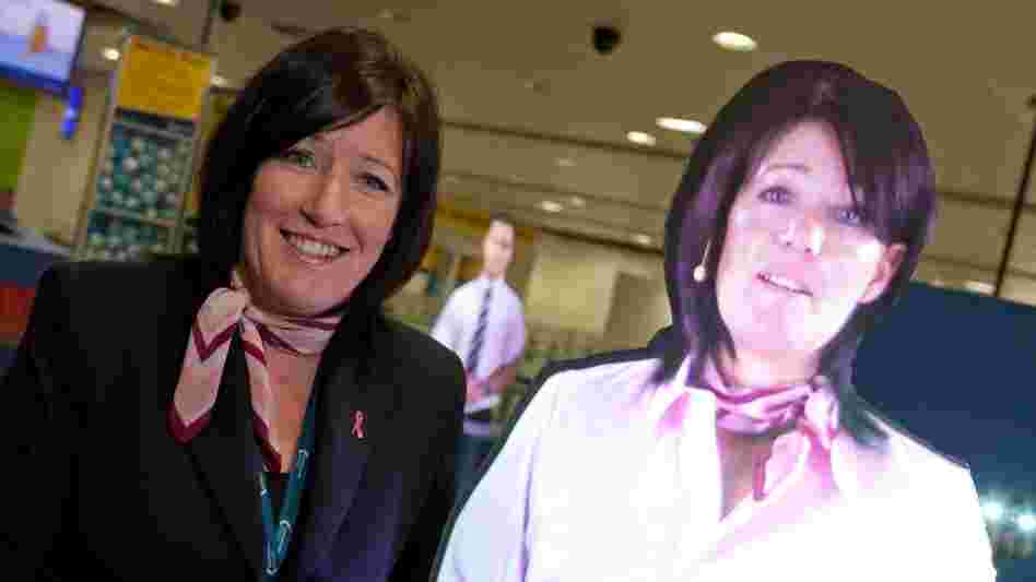 Julie Capper stands with her hologram at Manchester International Airport. Julie and her hologram work in the same area — which has created some confusion.