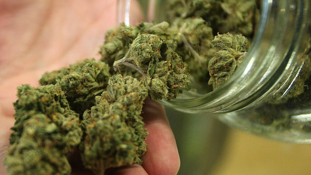 Marijuana buds tumble out of a jar.