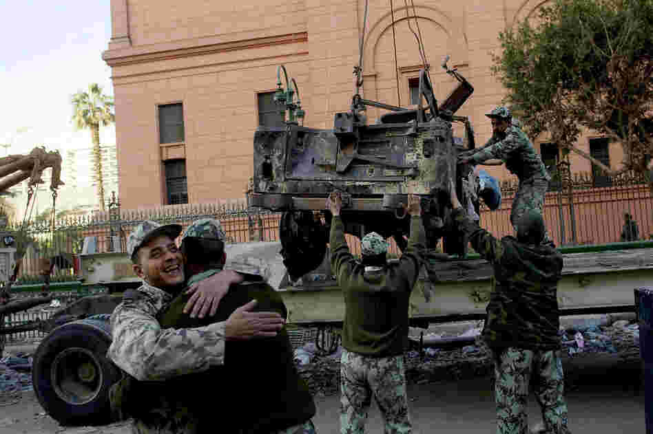 Soldiers hug as others remove the wreckage of a car burned during the anti-government protests in Cairo. 