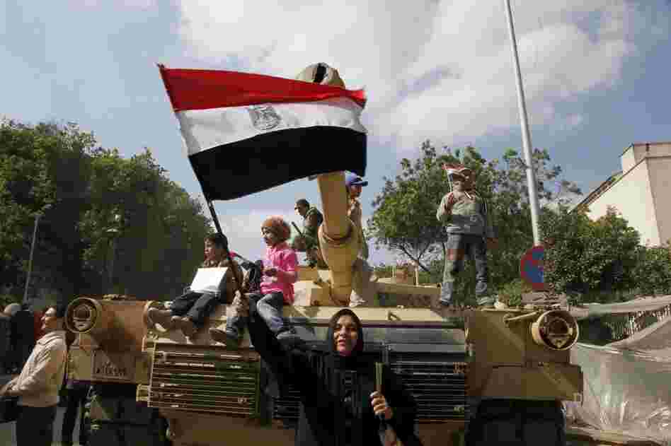An Egyptian woman waves the national flag in front of a tank. 
