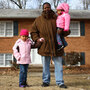 Robert  Adams carries his daughter Layla, 2, and walks with Lucy, 4, in front of their home in District Heights, Md. Adams grew up near the Anacostia Historic District  of Washington, D.C., but couldn't afford to buy a home  there for his family. He now lives in this suburb, a few miles away from his mother and  grandmother, who still live in the house where he grew up.